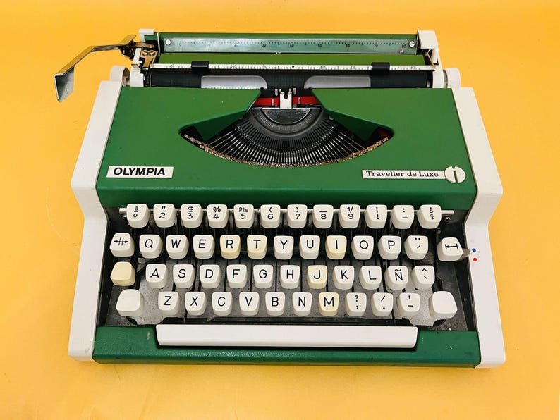 Green and white Olympia Traveller de Luxe typewriter on yellow background.